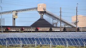 A train and a larger industrial plant sit behind a field of solar panels.