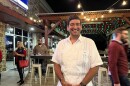 A man in a white guayabera shirt poses for a photo outside a bar.