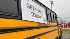 School bus with a banner hanging that reads "Get Hired Today"