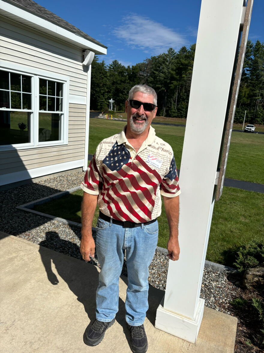 Epsom poll worker Bob McKechnie, a tan white man with grey hair and beard and sunglasses, wearing an American flag polo shirt and jeans.