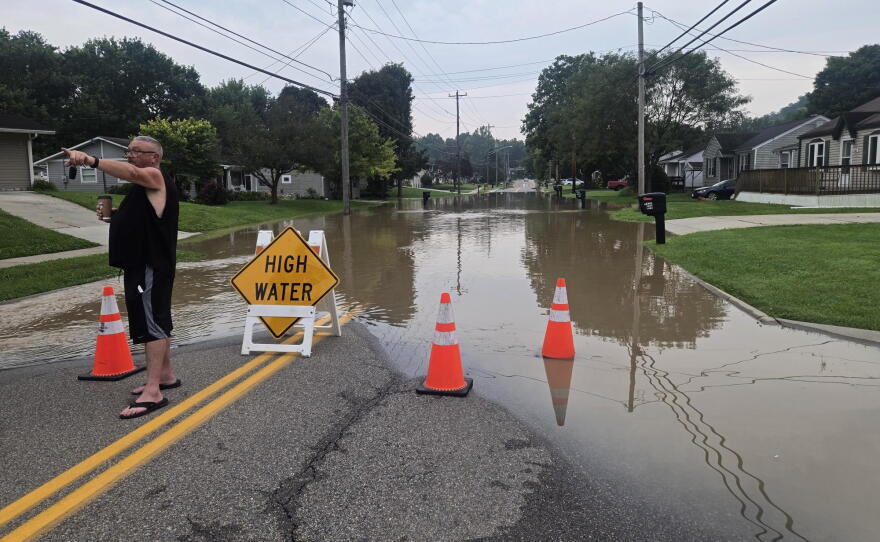 A man standing in front of a flooded street points to something off camera.