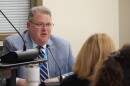 Man in suit, ties and glasses speaks during a board meeting.