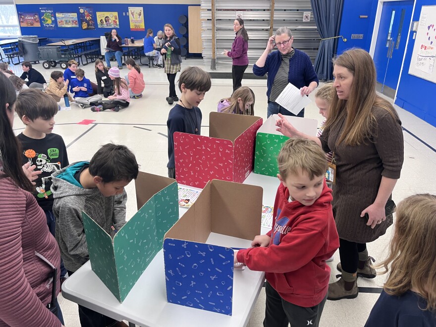 Elementary school kids filling out ballots at a table with cardboard ballot privacy booths