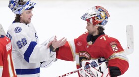 Two goalies shake hands, one in white jersey and the other in red