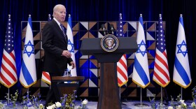 President Joe Biden walks to the podium to deliver remarks, with Israeli and American flags in the background.