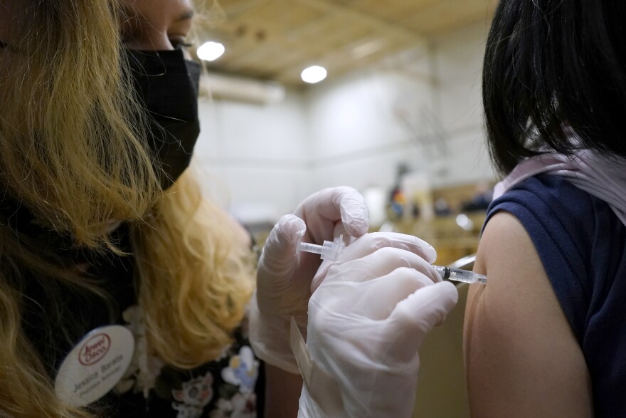 A healthcare worker administers a vaccine through a needle in the arm of a young girl.