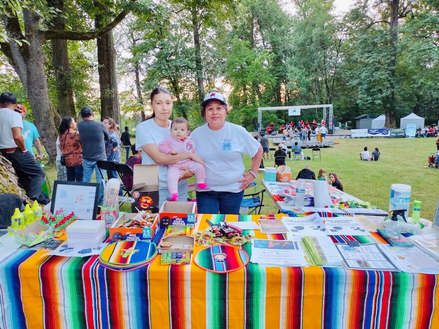 Mariela German Hernandez and another Escudo Latino volunteer stand in front of a colorful table. 