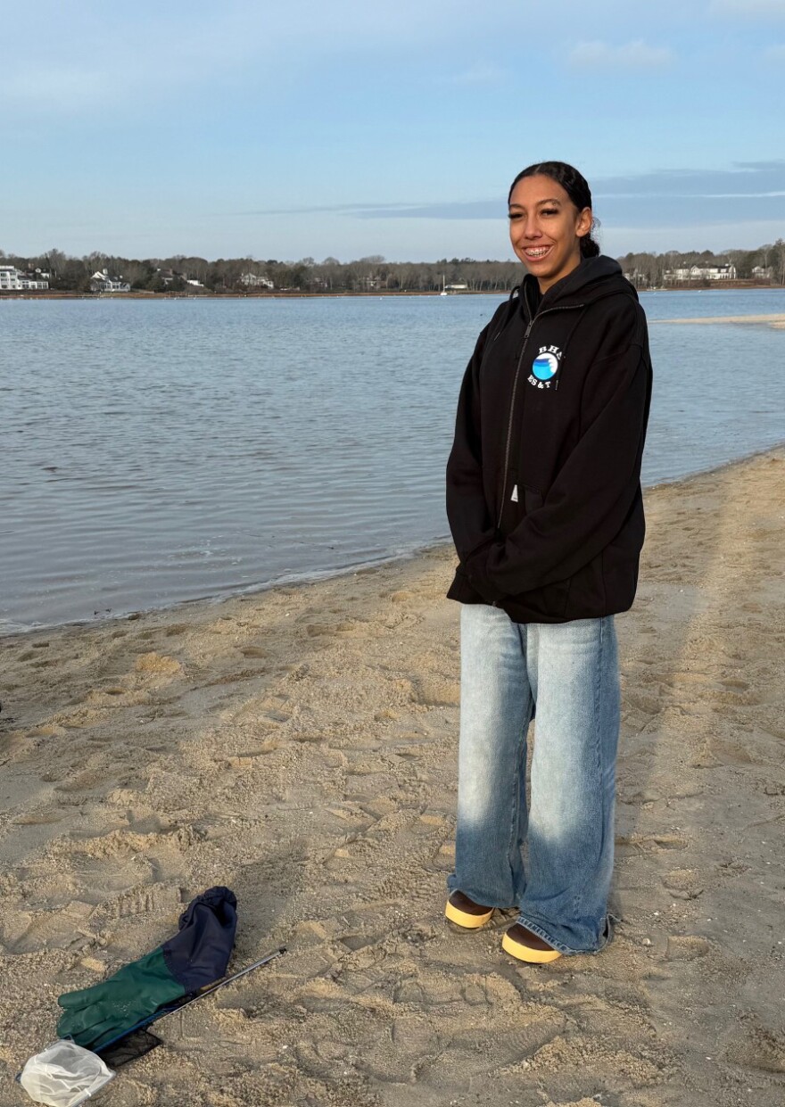 A student standing on a beach beside waterproof gloves and a small hand net
