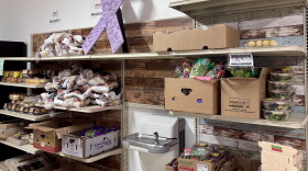 Boxes of vegetables and berries, bags of potatoes and containers of bakery items sit on shelves in a lit room.