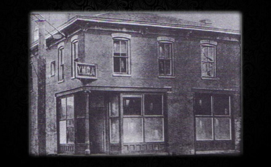 A black and white photograph of an old, two-story brick building with a sign reading "YMCA" above the ground level.