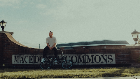 Brett Zupka sits on a brick wall with the Macedonia Commons sign on it