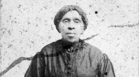 A black-and-white historical portrait of an African-American woman seated with a quilt square on her lap