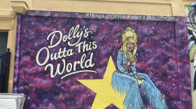 a mural of country singer Dolly Parton sitting on a yellow star with the words "Dolly's Outta This World."