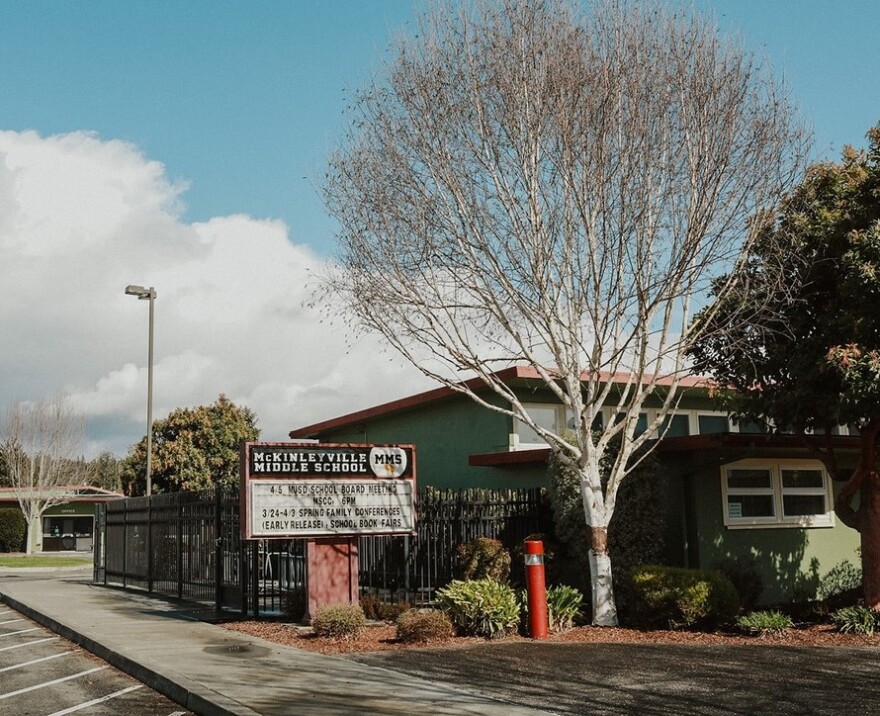 A green, single-story school building is shown, with trees and a sidewalk. 