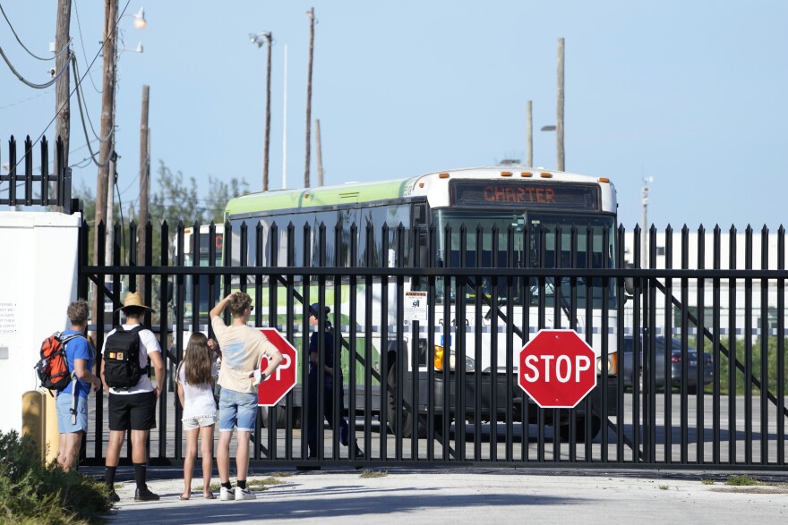 Onlookers watch as busses carrying Cuban migrants leave from U.S. Coast Guard Sector Key West facility, Thursday, Jan. 5, 2023, in Key West, Fla. Homeland Security officials said 337 migrants were taken Thursday by Coast Guard cutter from Dry Tortugas National Park on a 70-mile trip to Key West to be processed. (AP Photo/Wilfredo Lee)