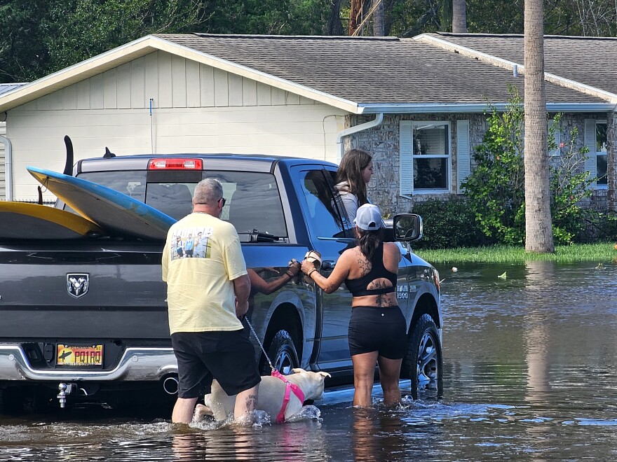 In the Big Tree Village neighborhood, South Daytona residents get a lift from a passing truck to cross a four-way stop with thigh-high, flood waters left behind Friday by Hurricane Milton.