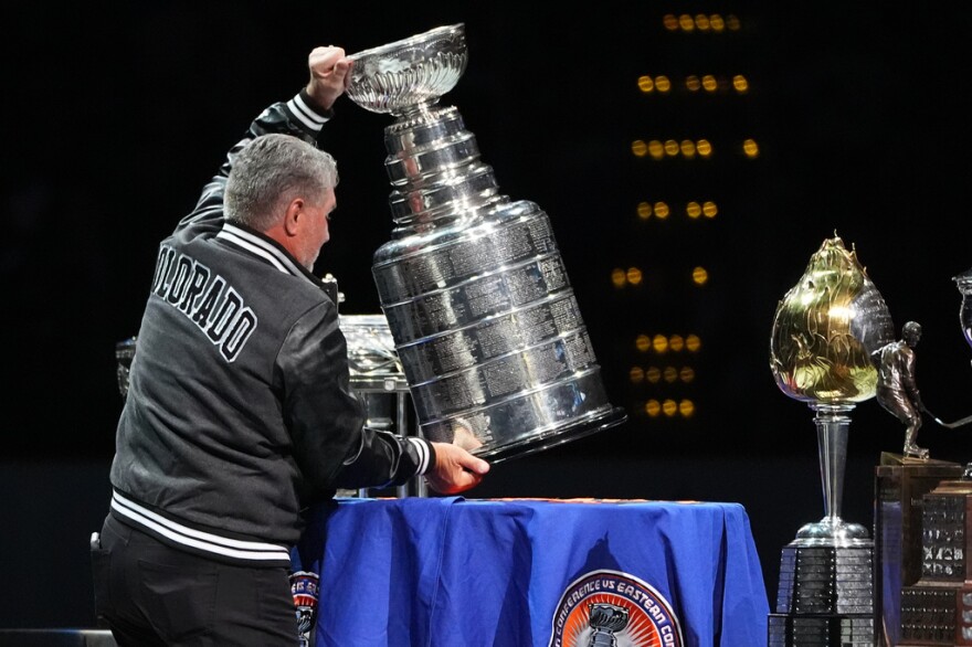 A man holds the Stanley Cup, a giant silver trophy, on a blue table.