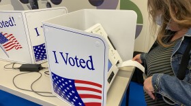 A woman places a ballot into a voting machine that sits inside an "I Voted" wrap-around box.