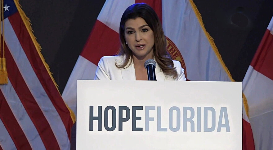 woman behind a podium that says Hope Florida speaks to an audience , american and florida flags are in the background 