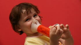 A child uses a spacer with an inhaler to treat asthma symptoms. Rising temperatures make the ozone and particle pollution that contribute to asthma problems worse.