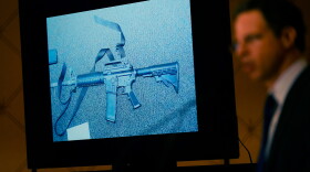 An image of the weapon used during the Newtown shooting is displayed while attorney Josh Koskoff speaks during a news conference in Trumbull, Conn., Tuesday, Feb. 15, 2022. The families of nine victims of the Sandy Hook Elementary School shooting have agreed to a $73 million settlement of a lawsuit against the maker of the rifle used to kill 20 first graders and six educators in 2012, their attorney said Tuesday.