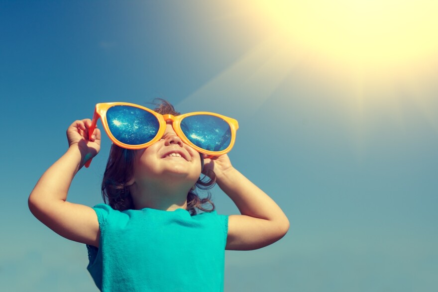 Happy little girl with big sunglasses looking at the sun 