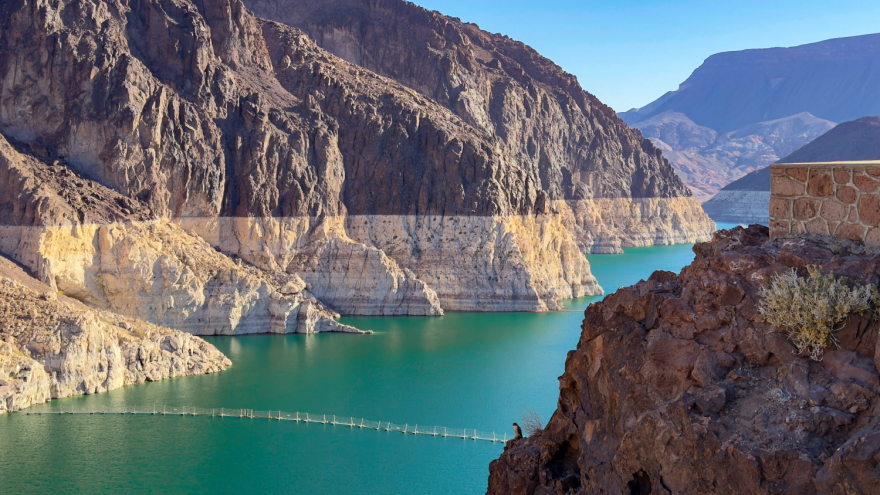 Photograph of Lake Mead. The rocky cliffs around the lake have a distinct line where it goes from dark to light, showing where the water line used to be. It's significantly higher than where the water currently sits.