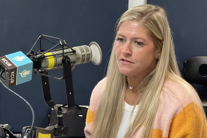 A woman sits inside a radio studio and is talking at a microphone.