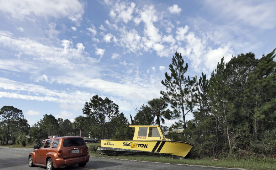 Motorists drive by a boat that was tossed onto the road when winds from Hurricane Hermine came ashore early Friday, Sept. 2, 2016, in Dekle Beach, Fla. Hermine was downgraded to a tropical storm after it made landfall, as it moves over Georgia, but the U.S. National Hurricane Center says winds are increasing along the Southeast coast and flooding rains continue. (AP Photo/Chris O'Meara)