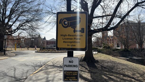 A bright yellow sign with a drawing of a security camera and the the words "High-Resolution License Plate Recognition In Use" written in black