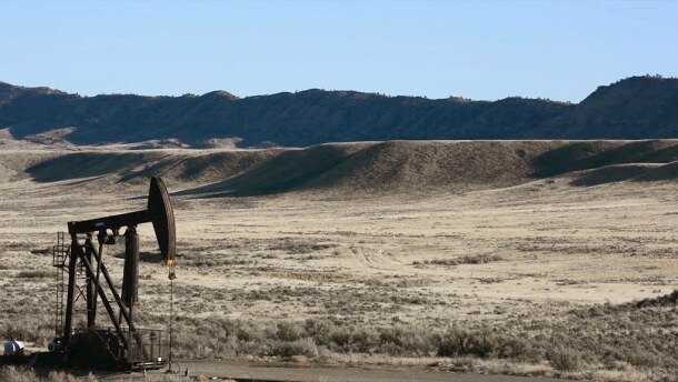 An oil well in front of golden grassy bluffs.