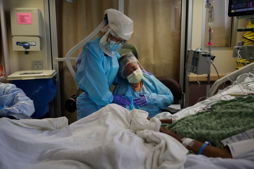 Nurse Michele Younkin (left). comforts Romelia Navarro as she sits at the bedside of her dying husband, Antonio Navarro, in St. Jude Medical Center's COVID-19 unit in Fullerton, Calif on July 31. Antonio was Younkin's first COVID-19 patient to pass on her watch.