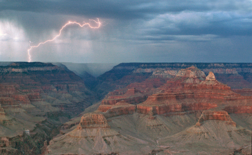 Elevated photo of the Grand Canyon with a lightning strike visible in the distance.
