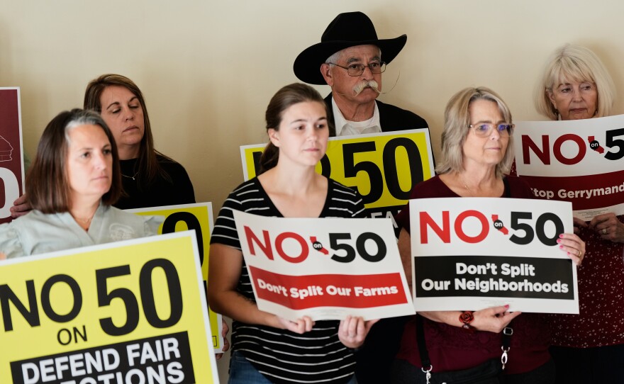 People hold up signs opposing Prop 50 during a press conference in Chico, Calif., Wednesday, Oct. 29, 2025.