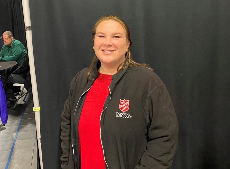 Woman in a red top and black Salvation Army jacket and a black backdrop