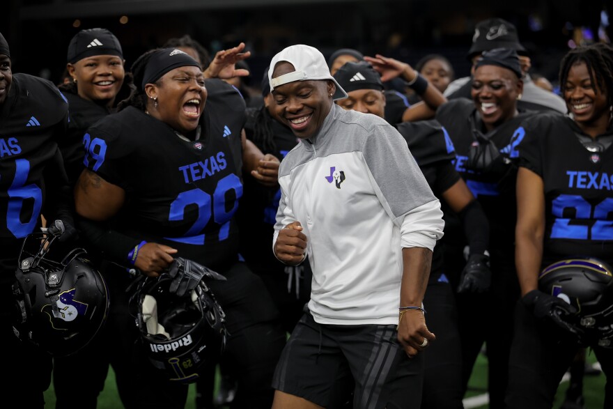A group of woman in tackle football gear surround their coach celebrating. 