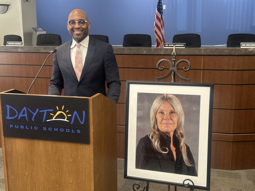Image, man standing at podium next to picture of woman. Dayton Public Schools Superintendent Dr. David Lawrence shares warm stories of working with friend and fellow board member Karen Wick.