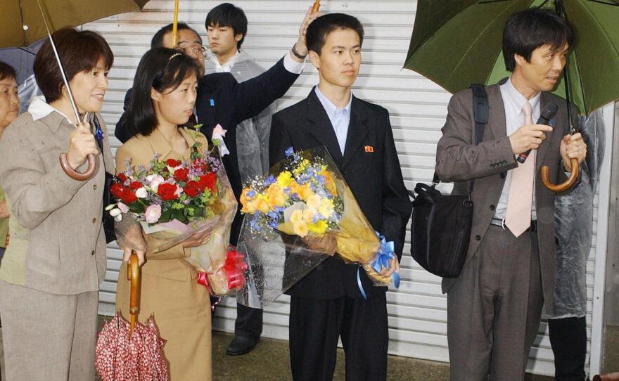 Former abductees Kaoru Hasuike (right) and his wife, Yukiko (left, holding umbrella), arrive at their home northwest of Tokyo with their two children (holding flowers) in 2004, after Japan won their release from North Korea.