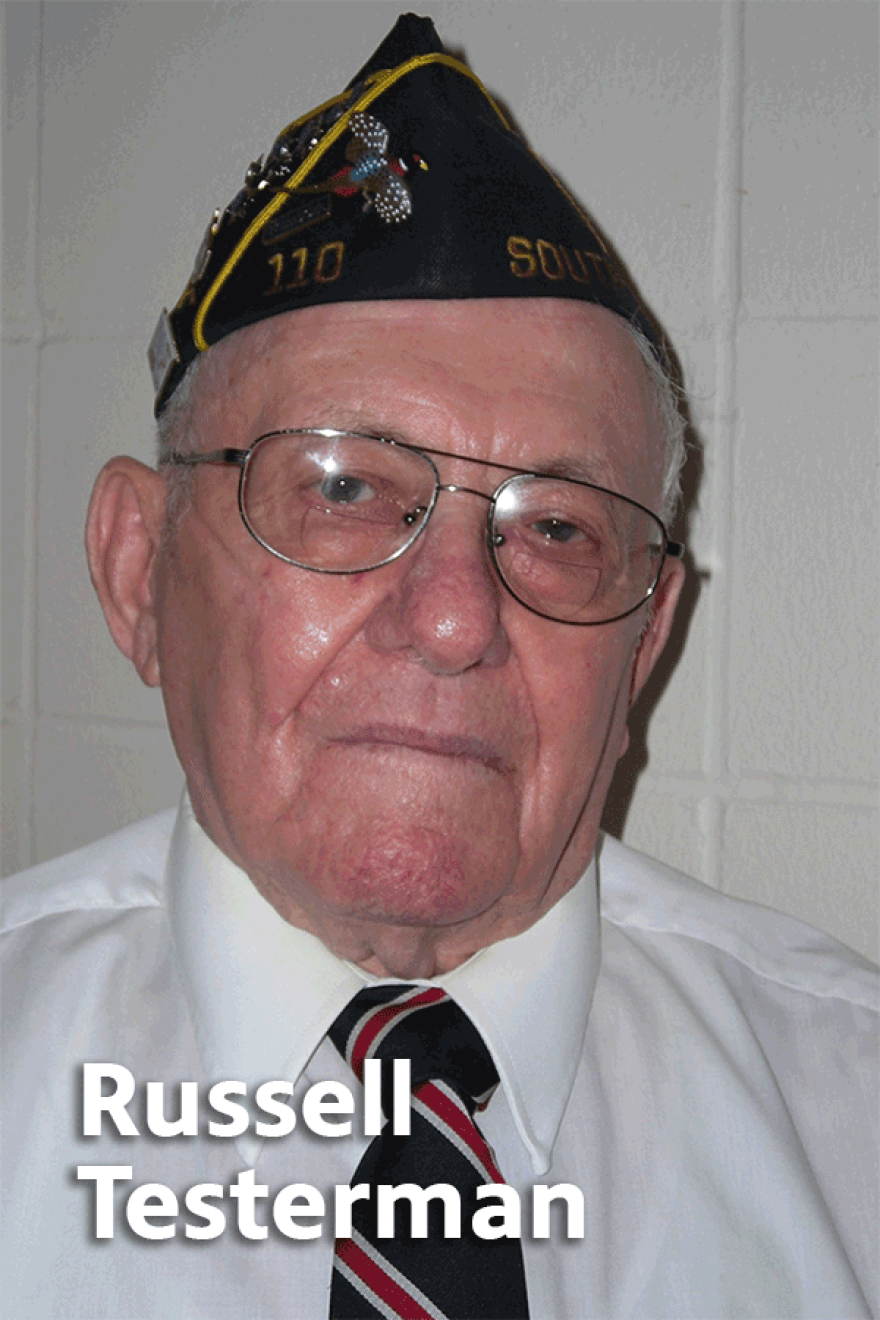 Elderly Russell Testerman wearing glasses, a white shirt with a black, white and red tie, and a black veteran's cap