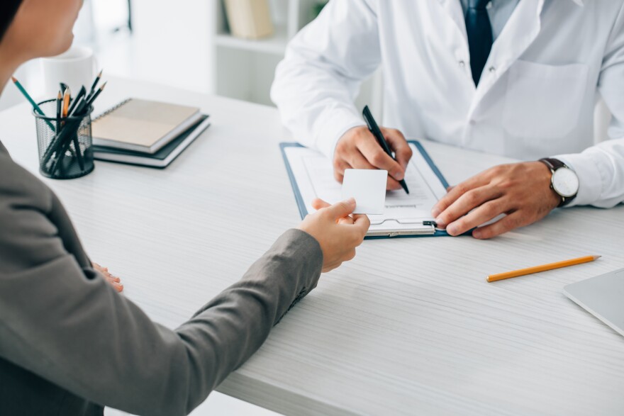 Woman hands health insurance card to doctor