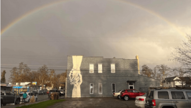 A building in the rain with a picture of two hands clasping painted on its side.