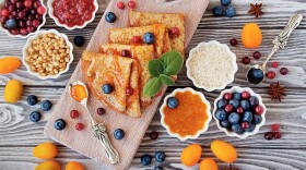 Wooden board with gluten-free crepes surrounded by jams and fruits