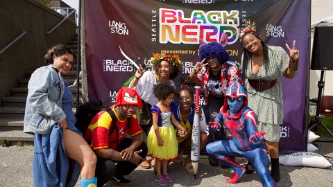 People in colorful costumes pose in front of a banner.