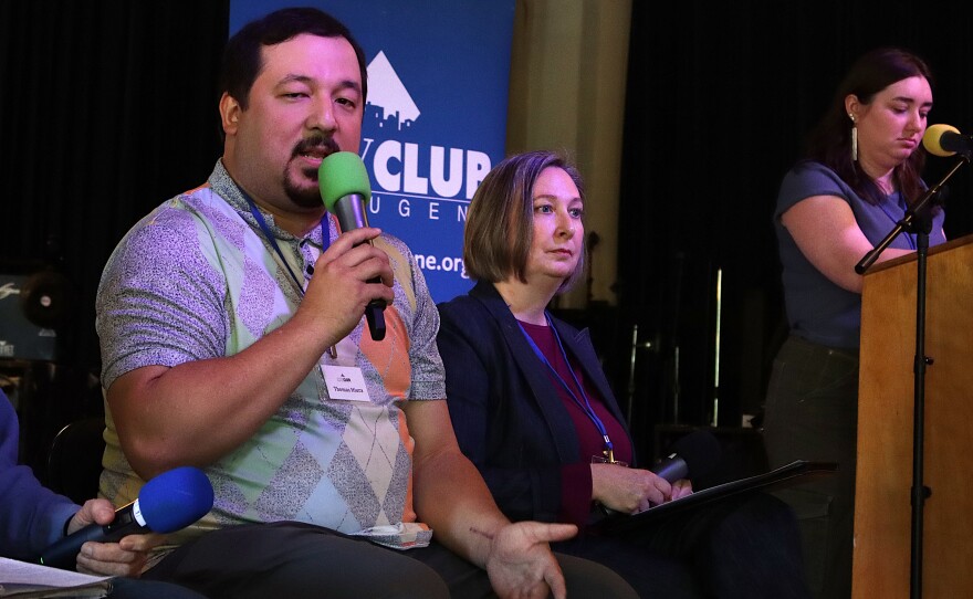 People sit on a stage in front of a City Club of Eugene banner.