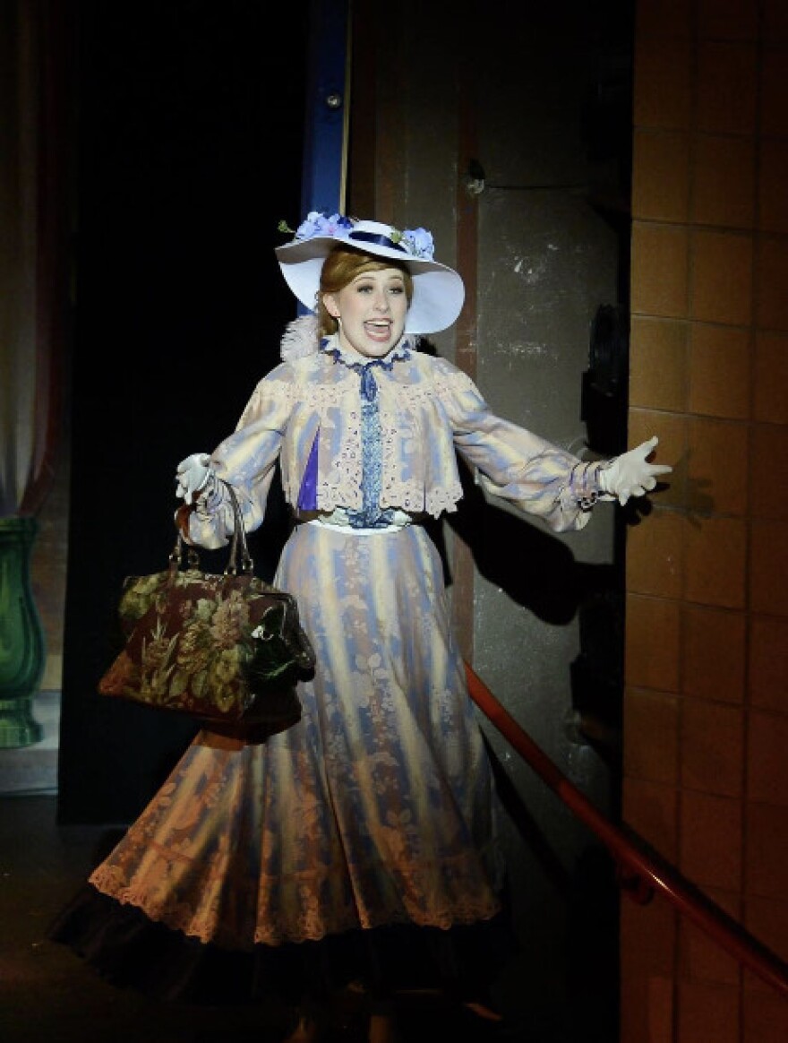 Girl in Victorian costume holding a bag and singing on stage