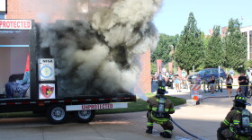 Two firefighters put out a fire in the "unprotected" section of the fire demonstration trailer with a hose.