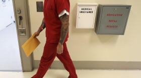 A person in an orange prison uniform walks down a hall. 
