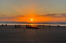 A whale lies on a beach. The sun is setting over the water. People are milling around in the background.