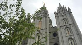 Mormon Temple partially obscured by tree with green leaves.