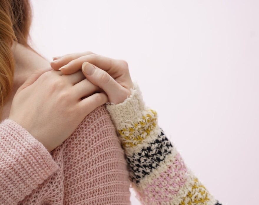 Woman reaching her hand back to her shoulder as another woman's hand is atop her hand in a comforting gesture